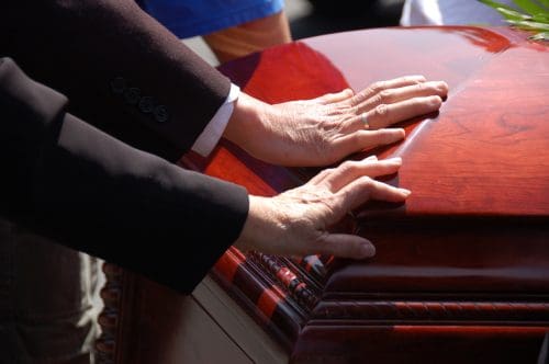 2 hands touching a closed wooden casket
