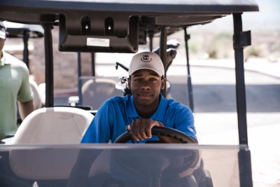 Black golfer driving a golf cart