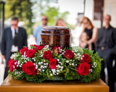 Burial urn decorated with flowers and people mourning in background at memorial service