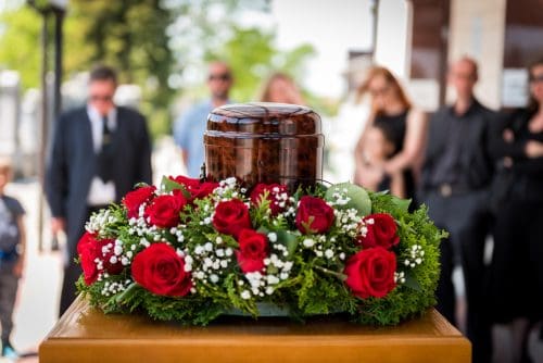 Burial urn decorated with flowers and people mourning in background at memorial service