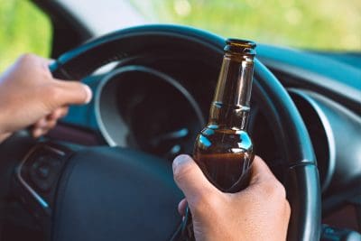 Closeup of drunk driver hands on the steering wheel with a bottle of beer. Driving under alcohol influence. 