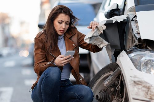 Displeased woman dialing for help after a car accident in the city