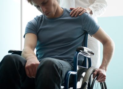 Female doctor consoling young man sitting in wheelchair