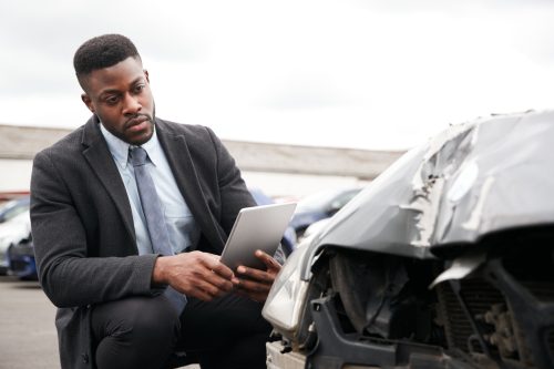 Male Insurance Loss Adjuster With Digital Tablet Inspecting Damage To Car From Motor Accident