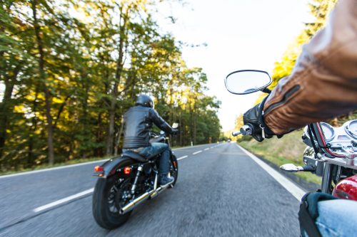 Man seated on a motorcycle on a forest road during sunrise