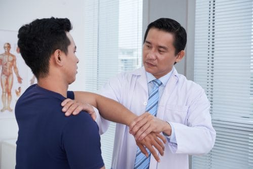 portrait of mature Asian traumatologist wearing white coat examining sporty young man