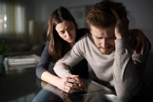 Sad man being comforted by his wife at home