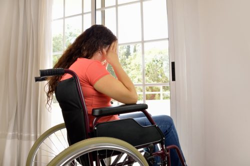 Sad woman sitting on wheelchair in empty room