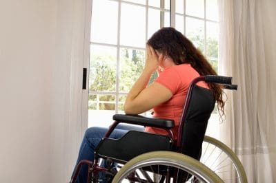 Sad woman sitting on wheelchair in empty room