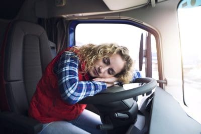 Sleepy and tired female truck driver sleeping over steering wheel inside truck vehicle cabin. People working overtime.