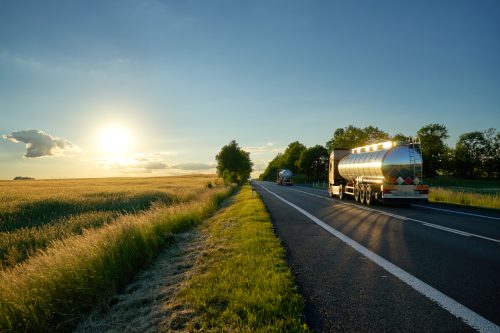 Trucks with chrome tank driving on road at sunset