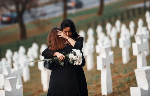 Two young women in black clothes visiting cemetery with many white crosses