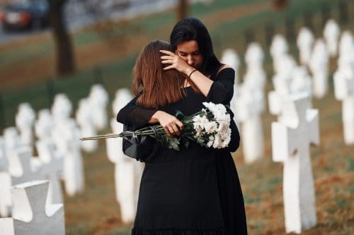Two young women in black clothes visiting cemetery with many white crosses