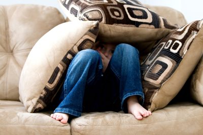 Young boy hiding under pillows on the couch
