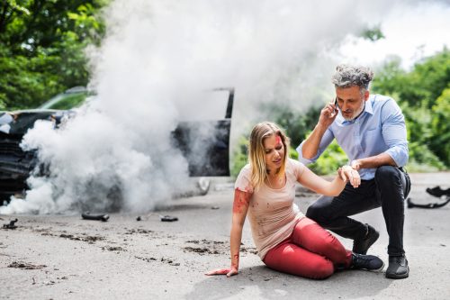 Young woman by the car after an accident and a man with smartphone, making a phone call