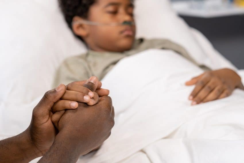 Close-up of father holding hand of his sick son and supporting him during disease